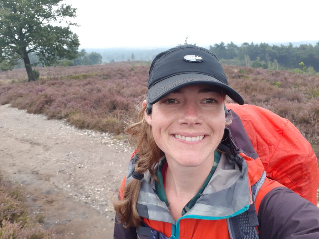 Selfie taken while hiking in the rain, wearing a black baseballcap, purple and orange rainjacket, and a red raincover for my backpack